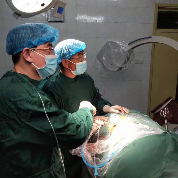 郑文杰（左）医生右手臂上，有一根塑料软管绕到背后，这是一根输氧管。他就是这样插着氧气管坚持做手术。 受访者供图 华龙网-新重庆客户端 发.jpg