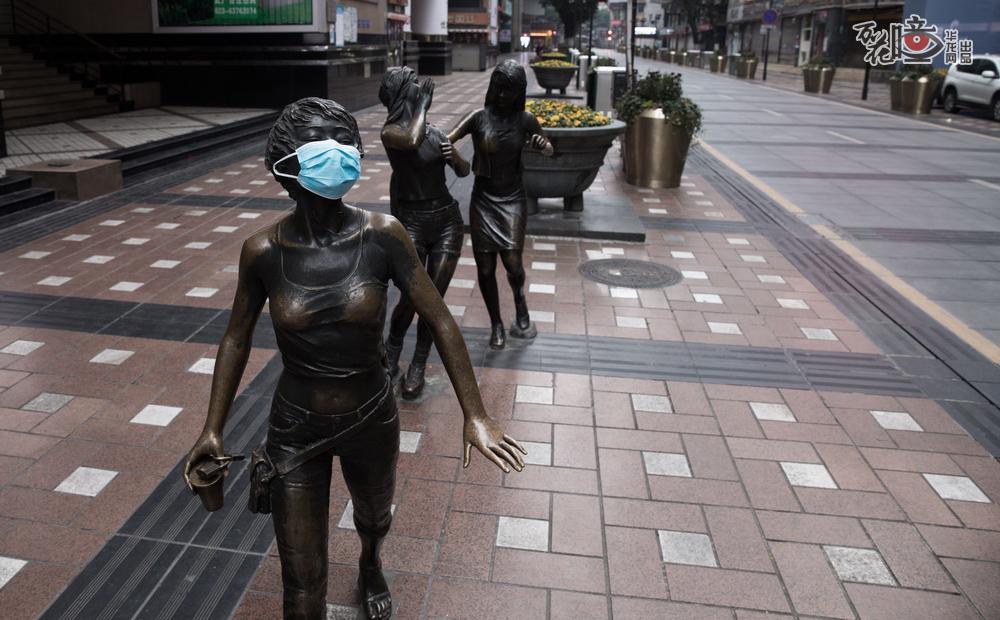 一个多月前，为提醒人们戴口罩防疫，摄影记者为街角的雕塑也戴上了口罩。位于重庆地标解放碑的八一路好吃街，三个逛街女孩的雕塑“站在”街角，没有了往日的观众。