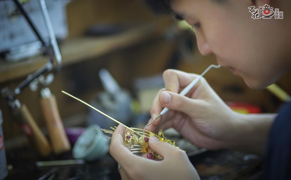 重庆潼南双江古镇一工作室，近1米8个头的刘扶伦弓着腰，眼神专注，细细地雕琢手中的饰品，那一根根纤细的花丝清晰可见。